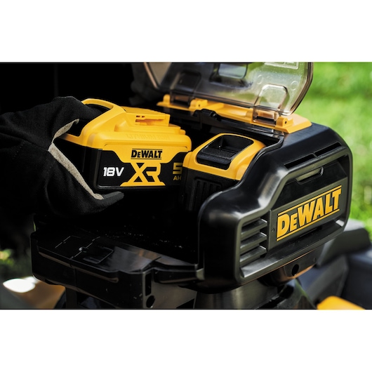 Gloved hand inserting DEWALT 18V XR battery into a DEWALT tool outdoors.