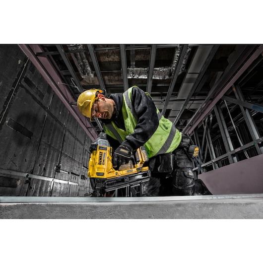 Worker using a DEWALT DCN890P2 nailer in a construction setting, wearing a helmet and safety vest.
