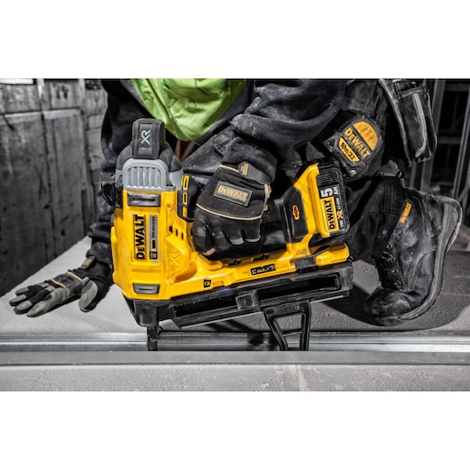 A DEWALT DCN890P2 cordless nailer in use by a worker wearing gloves and workwear on a construction site.
