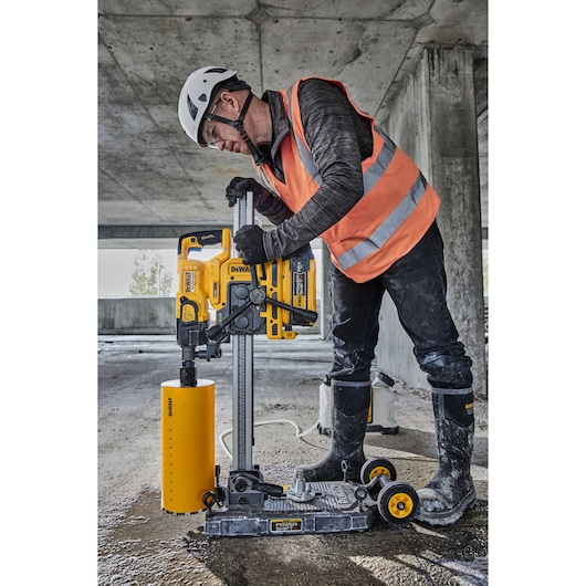 Worker uses a DEWALT DCPS151 core drill on a construction site. He wears safety gear and operates the yellow tool.