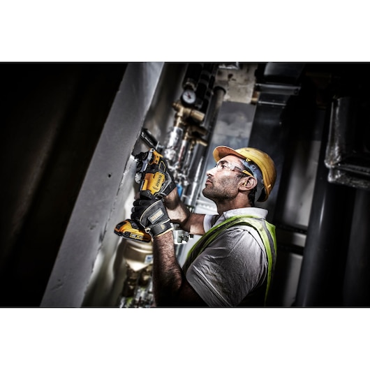 Worker uses a DEWALT DCS355D2 power tool on a wall at a construction site, wearing safety gear and gloves.