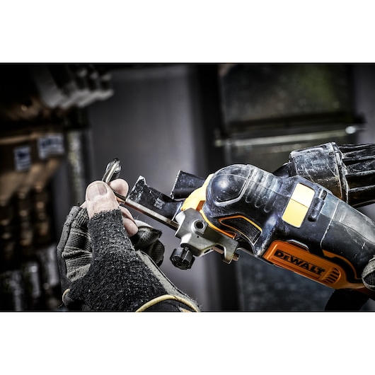 A gloved hand adjusts a Dewalt DCS355D2 cordless oscillating multi-tool blade in a workshop setting.