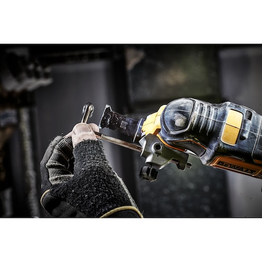 A gloved hand uses a DEWALT DCS355D2 oscillating tool to cut a metal object in a workshop setting.