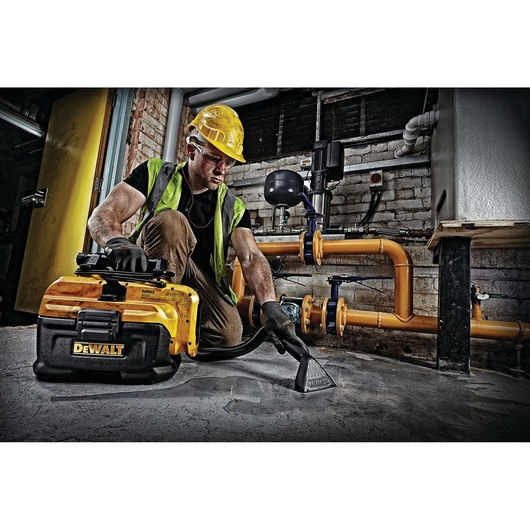 Worker uses a DEWALT DCV582 vacuum cleaner to clean a cement floor in an industrial setting.