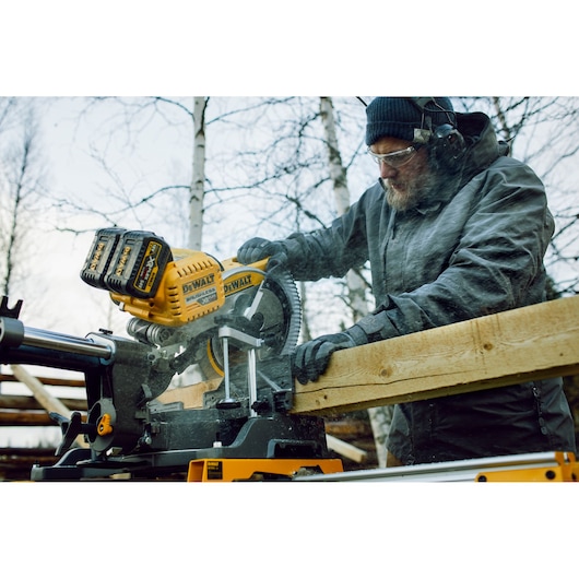 DEWALT DHS780T2 saw cutting wood outdoors, operated by a person wearing gloves and protective gear.