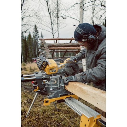 Person using a DEWALT DHS780T2 saw outdoors to cut wood, wearing safety gear and winter clothes.