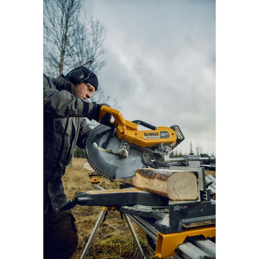 DEWALT DHS780T2 saw cutting a wooden log outdoors. Operator uses protective gear. Photography product.