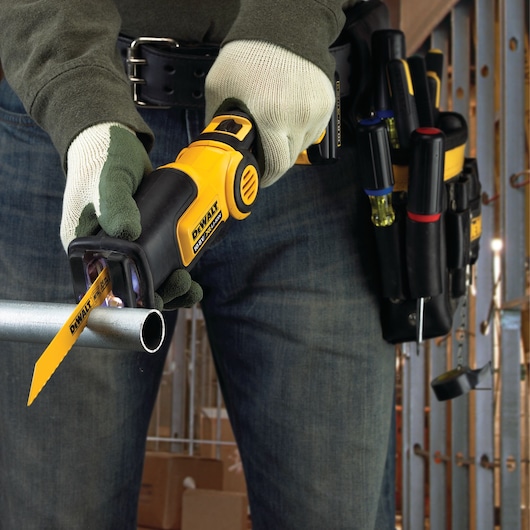 Person uses DEWALT reciprocating saw to cut a metal pipe; tool belt and gloves visible.