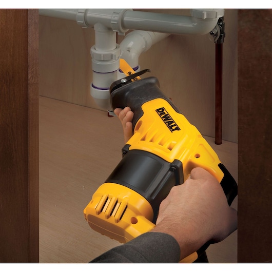 DEWALT reciprocating saw being used under a sink to cut plumbing pipes.