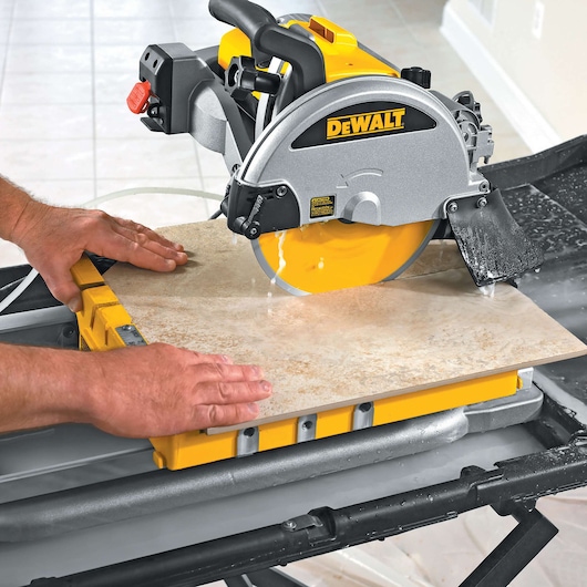 DEWALT tile saw cutting a ceramic tile with water cooling on a table, guided by hands.