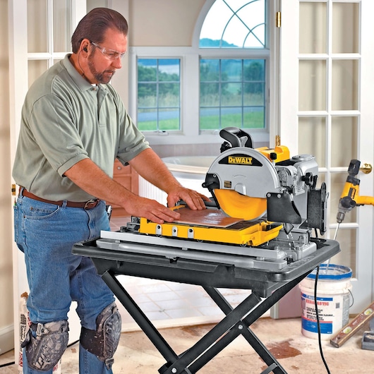 Person using a DEWALT DT3733 saw for tile cutting indoors, wearing knee pads and ear protection.