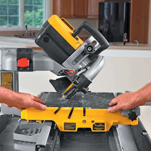 Hands guide a DEWALT tile saw cutting a stone slab indoors. Adjustable angle and safety features visible.