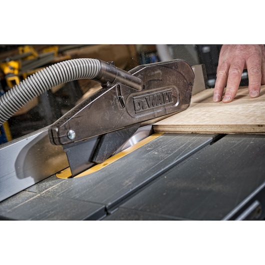DEWALT table saw cutting wood, safety guard in place, close-up of hand and saw mechanism.