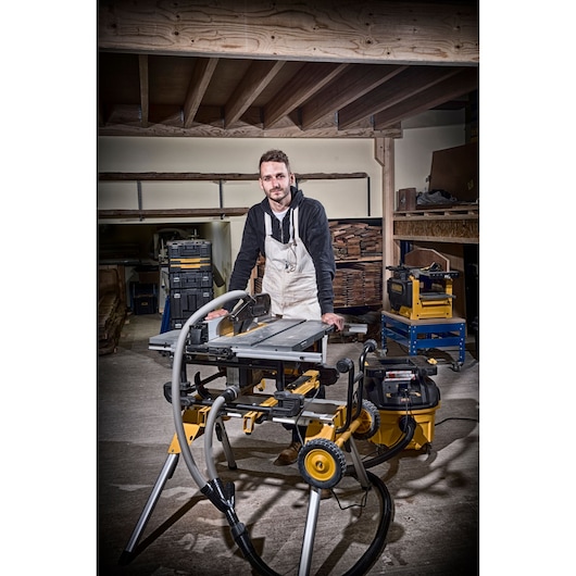 Person in workshop with DEWALT DT4351 saw on a stand and dust extraction system, surrounded by wood and tools.