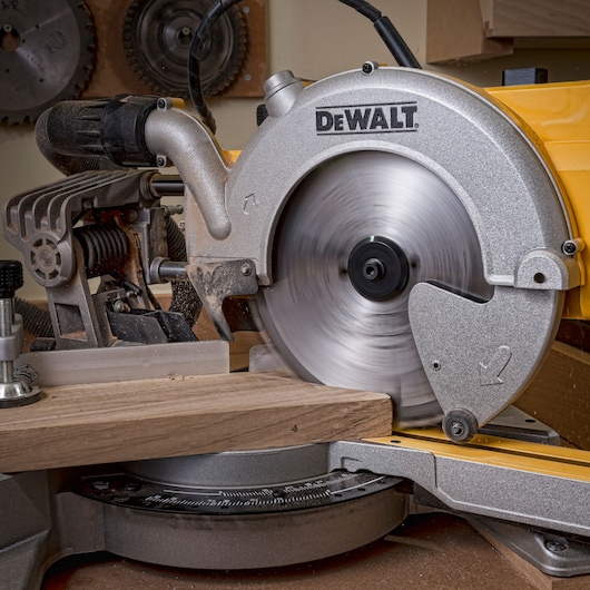 DEWALT DT4353 saw cutting wood in workshop, showing spinning blade and precise miter angle adjustment.