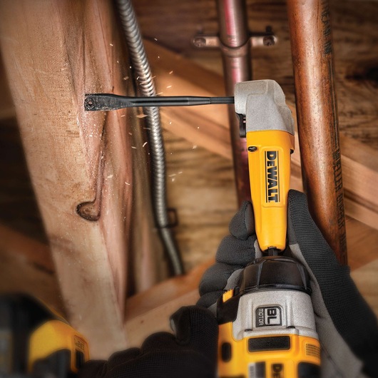 DEWALT drill with DT4765 flat drill bit drilling wood in a tight space, held by gloved hands.