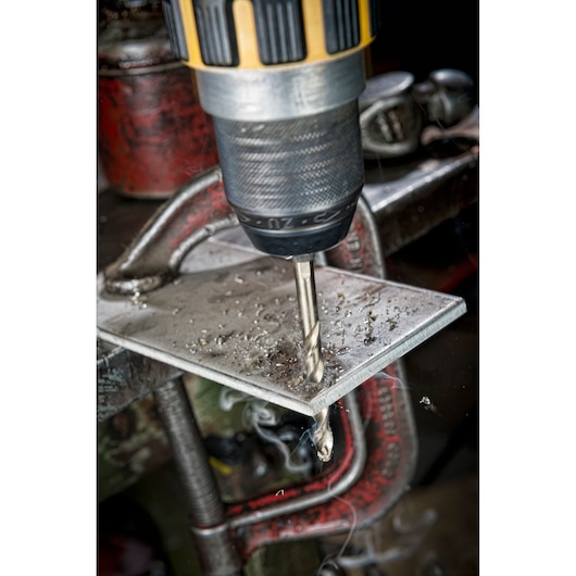 DEWALT drill bit DT4939 drilling through a metal plate held by a clamp, with metal shavings visible.