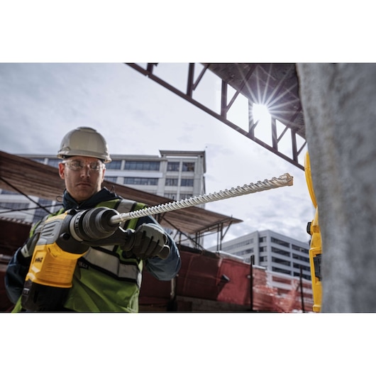 Worker holding DEWALT DT60810 drill bit at a construction site with buildings in the background.