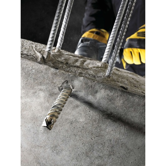 DEWALT drill bit boring through concrete with steel rebars, operated by worker wearing yellow gloves.