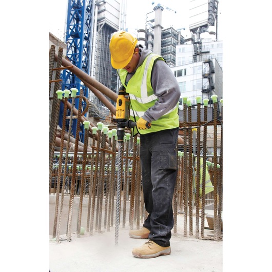 Worker uses DEWALT drill on construction site, wearing safety vest, helmet and gloves near rebar.