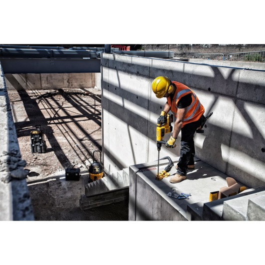 DEWALT DT60820, DT60820-QZ for photography. Worker drills concrete at construction site wearing safety gear.