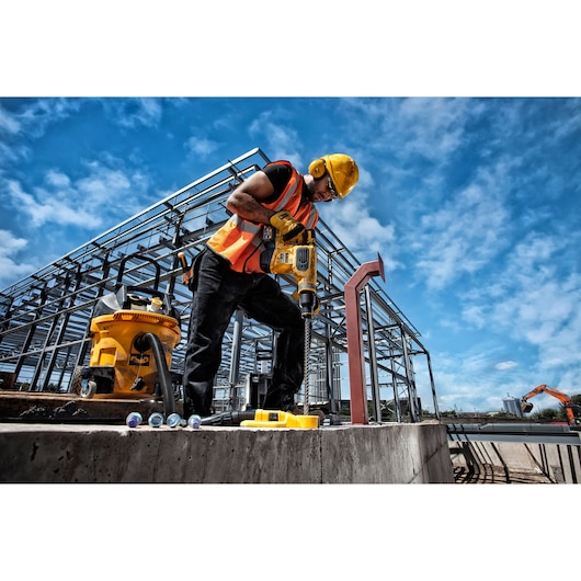 Worker uses DEWALT drill at construction site with steel frame and blue sky in the background.