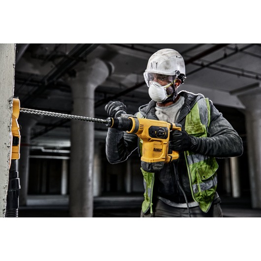 Person uses a DEWALT rotary hammer drill with DT60827 bit on concrete at a construction site.