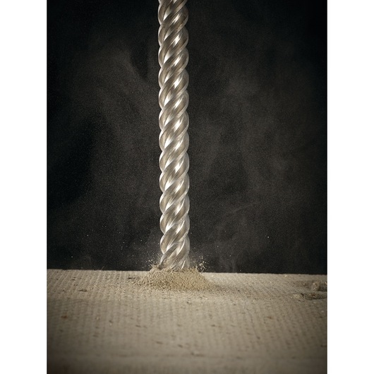 Close-up of a DEWALT drill bit penetrating a concrete surface, producing dust and debris.