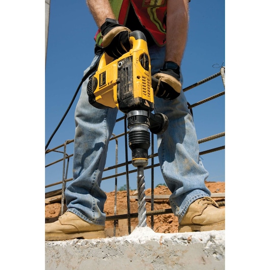 Person uses a DEWALT hammer drill to drill into concrete at a construction site outdoors.