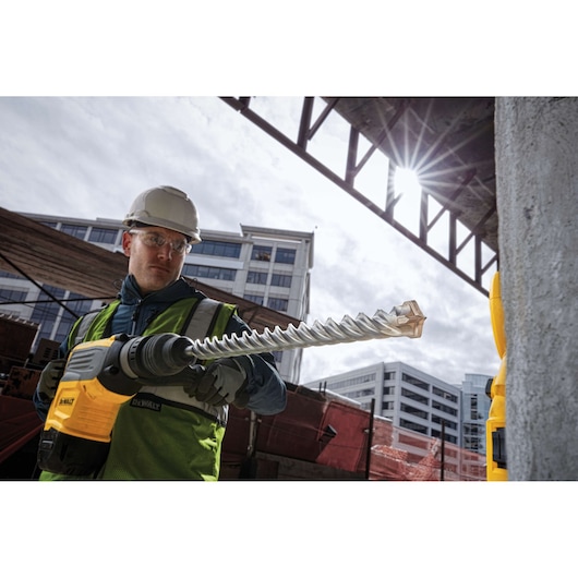 Worker using a DEWALT drill with DT60844 bit on a construction site, wearing safety gear and helmet.