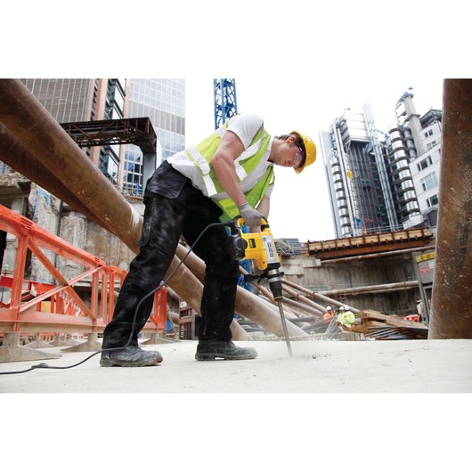 Worker using a DEWALT DT6825 tool to drill concrete at a construction site with buildings in the background.