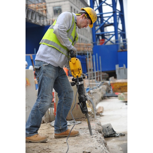 Worker uses a DEWALT DT6929 drill on construction site, wearing safety gear and breaking concrete.