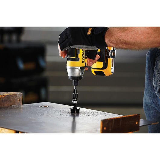 A person uses a DEWALT drill to make a hole in a metal sheet, wearing gloves for protection.