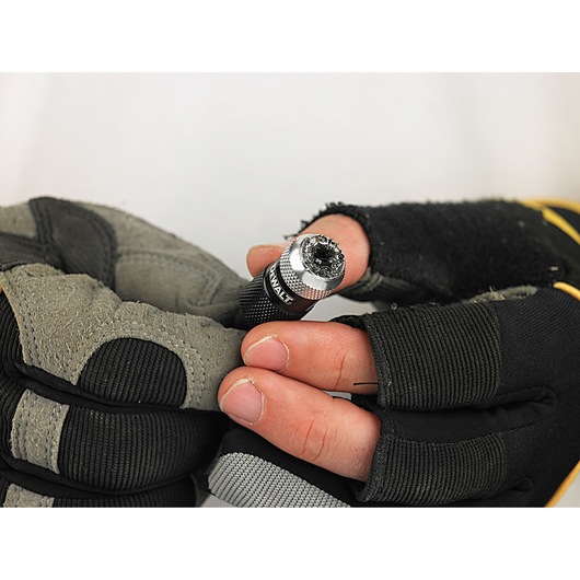 Gloved hands holding a DEWALT drill bit holder with used drill bit, close-up view.
