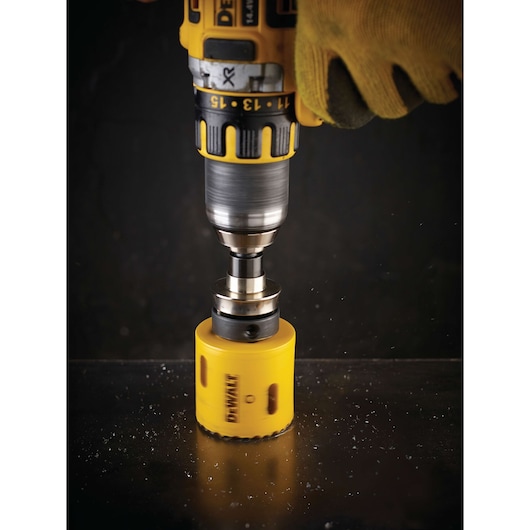 DEWALT drill with yellow hole saw cutting into metal surface, operated by a gloved hand.
