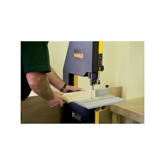 Person operating DEWALT bandsaw to cut wood in a workshop setting.