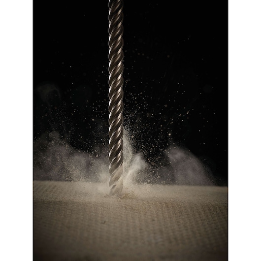 Close-up of a metal drill bit cutting into a surface, with dust and debris flying in all directions.