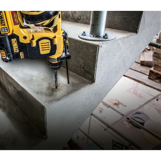 DEWALT drill in use, drilling into a concrete staircase step at a construction site.