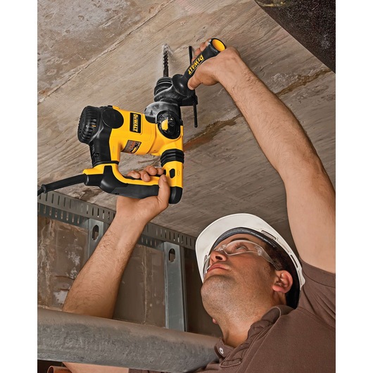 Person using a DEWALT DT8938 hammer drill to drill into a concrete ceiling at a construction site.