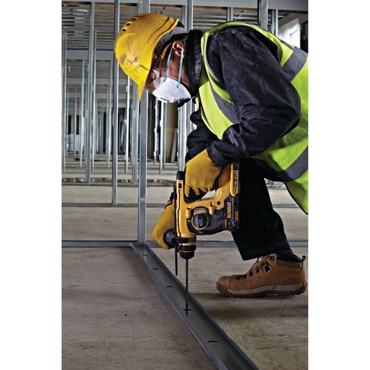 Worker in safety gear uses a DEWALT drill to make holes in a metal frame at a construction site.