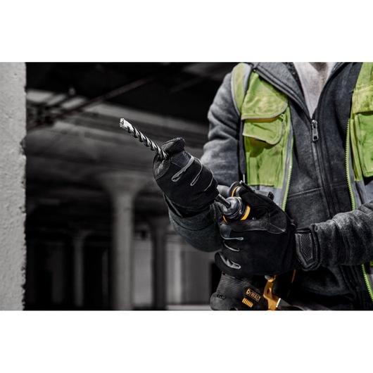 Person wearing gloves uses a DEWALT drill with a spiral bit in an industrial environment.