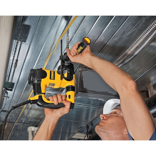 Person uses a DEWALT power drill to drill into a metal ceiling, showing tool and arms in action.