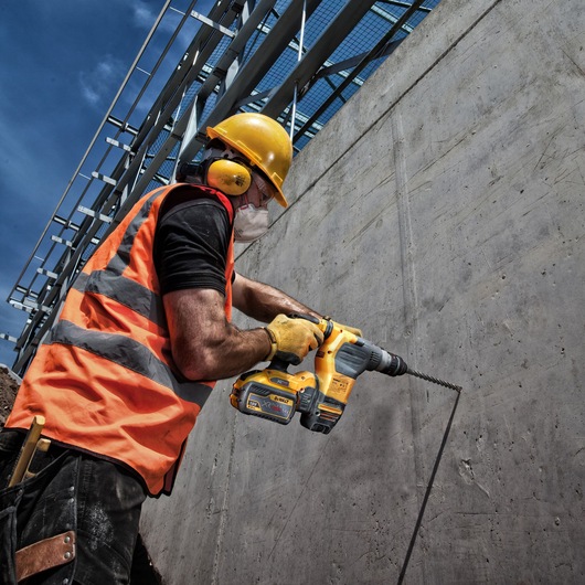 Worker using DEWALT DT9580, DT9580-QZ drill on concrete wall at construction site. Photography product.