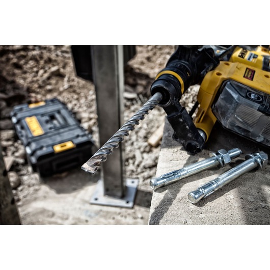 DEWALT drill with masonry bit and anchors on concrete, toolbox in background at construction site.