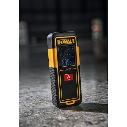 DEWALT DW033 laser distance measurer with a digital screen, yellow and black, standing on a concrete floor.