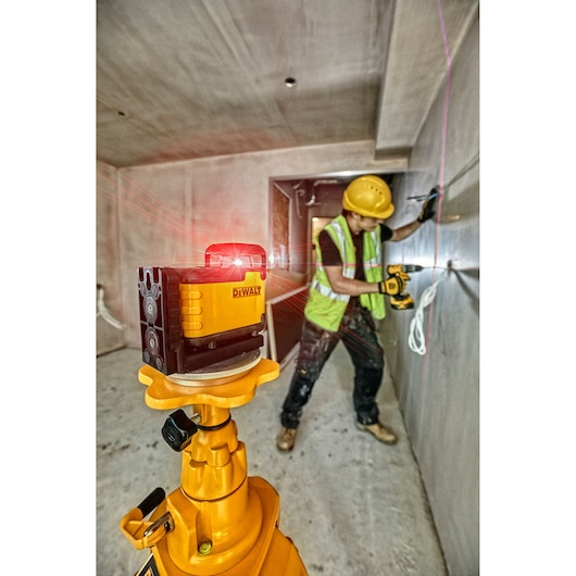 DEWALT laser level projects red lines in construction room; worker in safety gear uses power tool near wall.