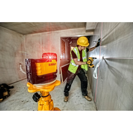DEWALT laser level projects red lines; worker uses drill on wall at construction site.