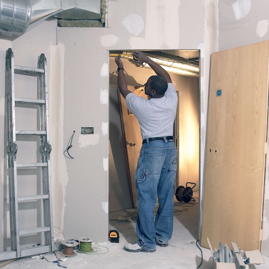 Person using DEWALT DW0822CG, DW0822 on a construction site with ladder, cables, and unfinished wall.