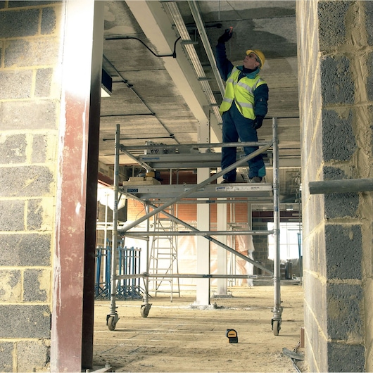 DEWALT DW0822CG, DW0822 laser on floor at construction site; worker uses scaffolding and safety gear.