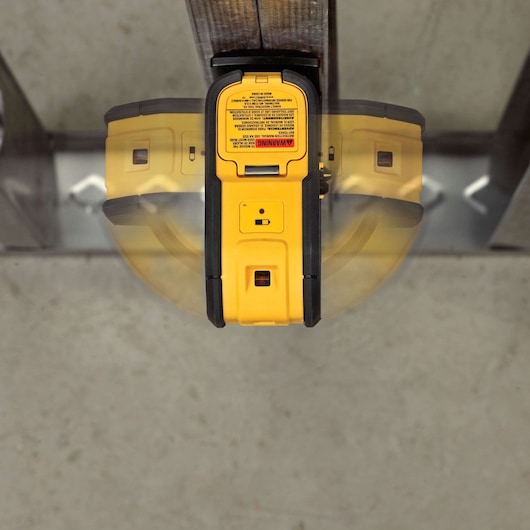Top view of a DEWALT DW083K laser level tool attached to a metal surface, showing its yellow and black design with adjustment controls and warning label visible.